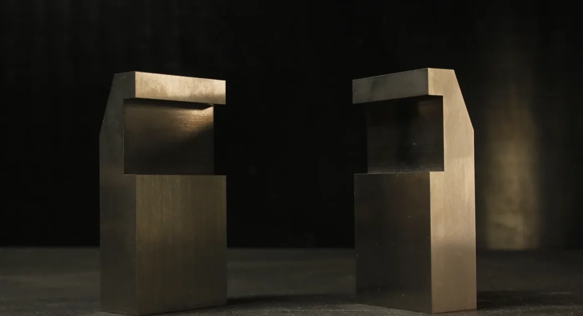 Two tungsten bucking bars with mirrored notched, stepped profiles facing each other, showing the offset geometry that clears an edge or flange