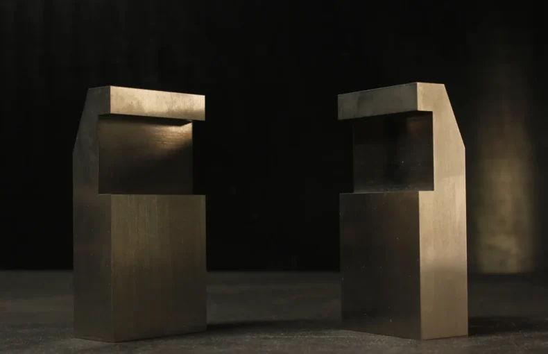 Two tungsten bucking bars with mirrored notched, stepped profiles facing each other, showing the offset geometry that clears an edge or flange