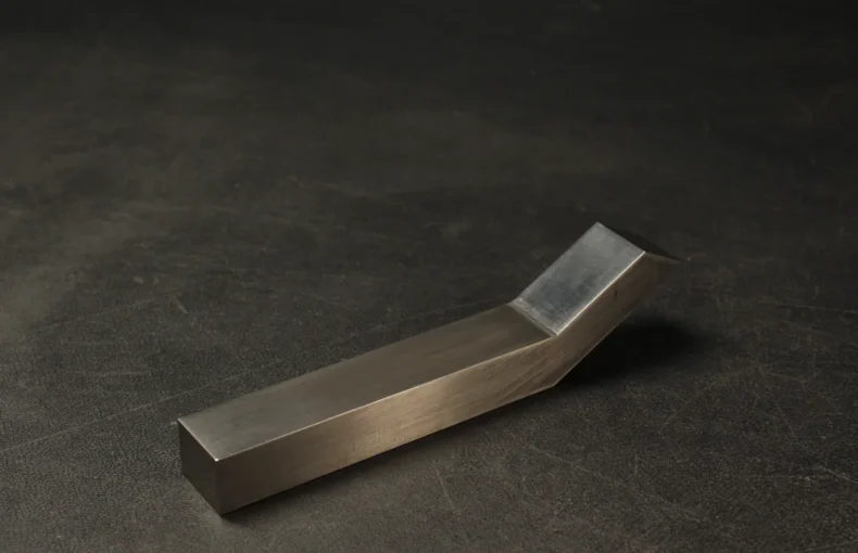 Offset tungsten bucking bar on a steel bench, polished working face catching the light, used to back solid rivets